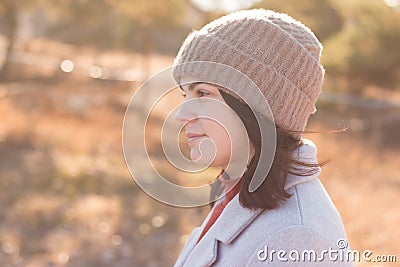 A serious girl in a knitted hat stands against a background and a coat against the backdrop of an autumn pale park landscape Stock Photo