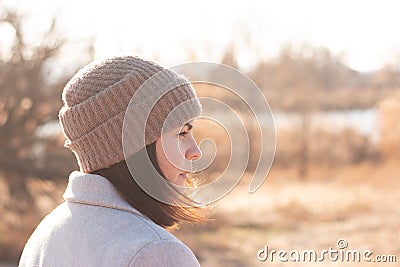 A serious girl in a knitted hat stands against a background and a coat against the backdrop of an autumn pale river landscape Stock Photo