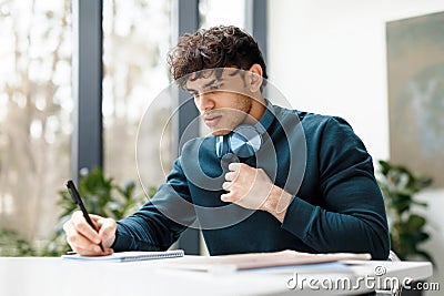 Serious guy doing his home assigment looking attentively in copybook and writing info, sitting in university audience Stock Photo
