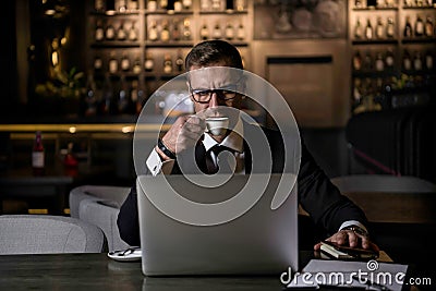 Serious handsome elegant caucasian businessman sitting at restaurant working on his laptop and drinking coffee Stock Photo