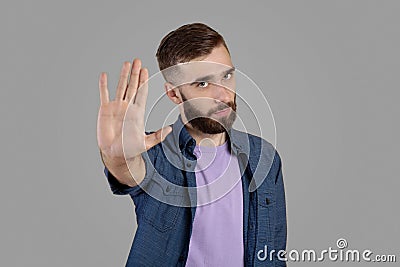 Serious hipster guy gesturing STOP, showing palm to camera over grey studio background Stock Photo