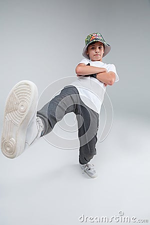 A serious little boy stands with arms crossed on chest and has one foot in front of him. On a gray background. Stock Photo