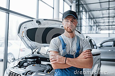 Serious look. Employee in the blue colored uniform stands in the automobile salon Stock Photo