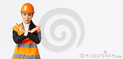 Serious-looking fed up asian female boss, construction manager in safety helmet showing cross gesture to stop, prohibit Stock Photo