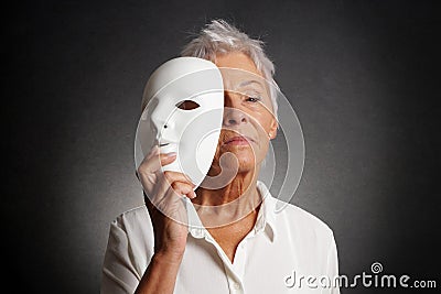 Serious older woman revealing face behind mask Stock Photo