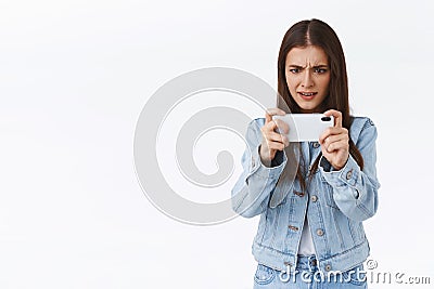 Serious-looking pressured and focused, determined brunette girl trying pass difficult level on mobile game, playing Stock Photo