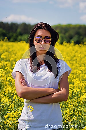 Serious lovely brunette in sunglasses stay in rapeseed field. Spring. Stock Photo