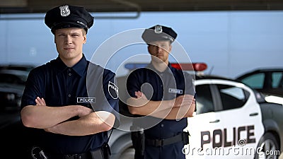 Serious male officers standing with hands crossed against police car background Stock Photo