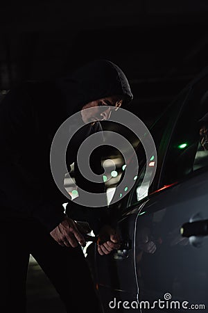 serious male robber in black hoodie intruding car Stock Photo