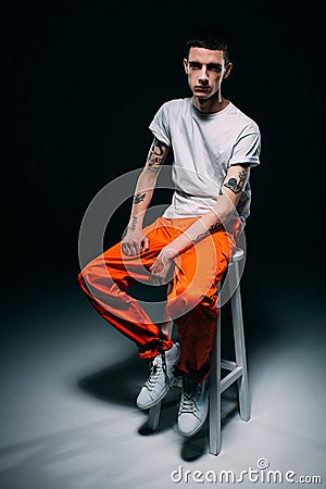 Serious man in orange uniform with cuffs on legs sitting on stool Stock Photo