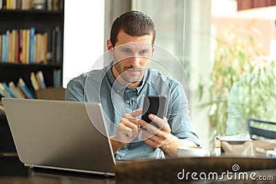 Serious man using smart phone and laptop in a bar Stock Photo