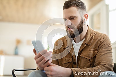 Serious Man Using Smartphone Wearing Earbuds Earphones At Home Stock Photo