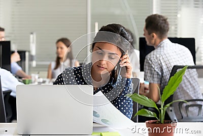 Serious millennial indian woman employee talking on phone in off Stock Photo