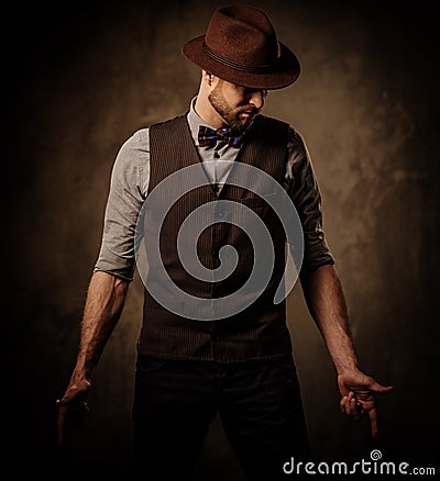 Serious old-fashioned man with hat posing on dark background. Stock Photo