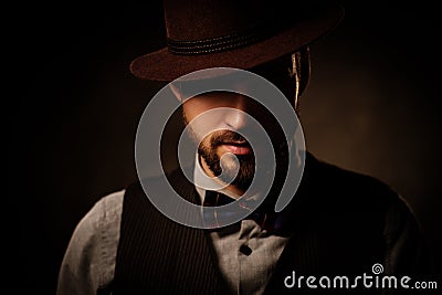 Serious old-fashioned man with hat posing on dark background. Stock Photo