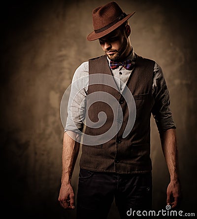 Serious old-fashioned man with hat posing on dark background. Stock Photo