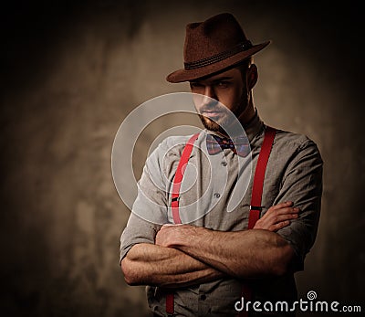 Serious old-fashioned man with hat wearing suspenders and bow tie, posing on dark background. Stock Photo