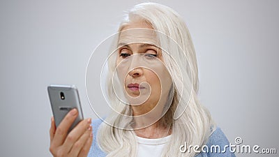 Serious old woman looking cellphone indoors. Senior lady searching news inside. Stock Photo
