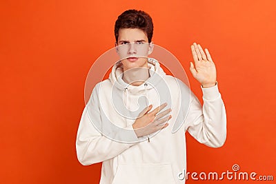 Serious patriotic male in white sweatshirt with hood holding hand on heart, juryman swearing to speak truth in court, honor and Stock Photo