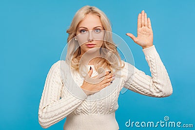 Serious patriotic woman with curly blond hair raising one arm and putting on chest another making oath, swearing Stock Photo