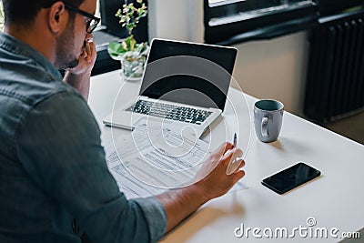 Serious pensive thoughtful focused young casual businessman or entrepreneur in office filling income tax return papers documents Stock Photo