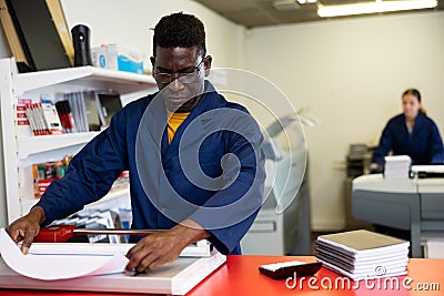 Serious print shop worker cuts paper on professional cutter Stock Photo