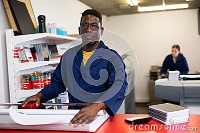 Serious print shop worker cuts paper on professional cutter Stock Photo