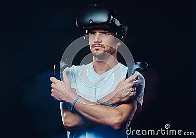 Serious pro gamer wearing virtual reality glasses and holds joysticks, posing with crossed arms. Stock Photo