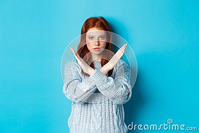 Serious redhead girl looking confident, showing cross gesture to stop and forbid action, standing over blue background Stock Photo