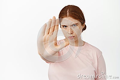 Serious redhead woman extend her hand to stop, saying no, furrow eyebrows determined to prohibit, forbid smth bad Stock Photo