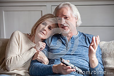 Serious senior couple embracing talking watching tv together at Stock Photo