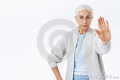 Serious and strict old woman, grandmother forbid, stretch arm forward in stop, rejection or prohibition gesture, look Stock Photo