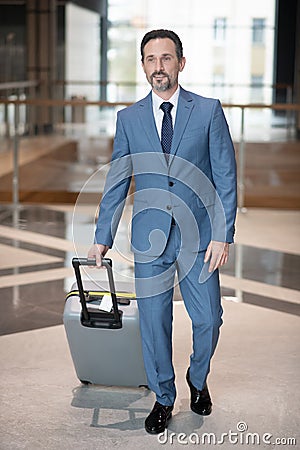 Serious successful businessman walking with luggage in the hotel Stock Photo