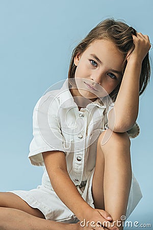 Serious little girl in a white thick romper suit sitting on the floor Stock Photo