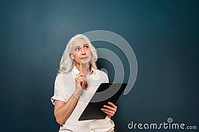 Serious thinking mature old woman writing notes in clipboard. Stock Photo