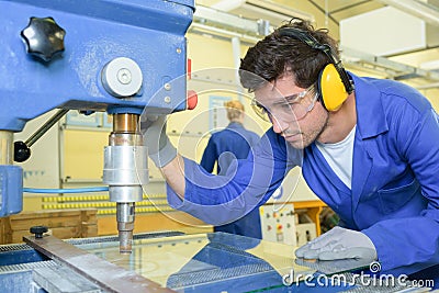 Serious trainees focused on drilling metal piece with professional machinery Stock Photo