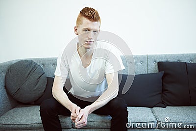 The serious type. A caucasian ginger sitting on a couch looking at the camera. Stock Photo