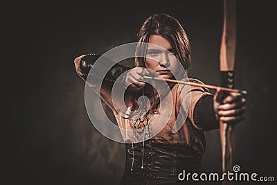 Serious viking woman with bow and arrow in a traditional warrior clothes, posing on a dark background. Stock Photo