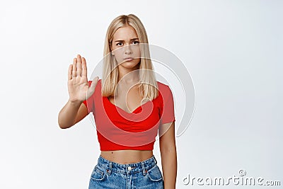 Serious woman looks concerned, shows stop prohibit gesture, saying no, disapprove something, standing over white Stock Photo