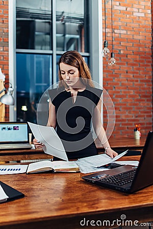 Serious woman reading papers studying resumes standing at work desk in stylish office Stock Photo