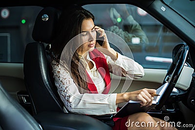 Serious woman successful business owner in formal wear checks in textbook the employment schedule and talking via mobile phone Stock Photo