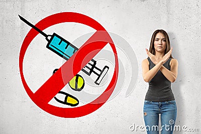 Serious young girl with hands crossed, standing against wall with picture of syringe and some meds enclosed in red Stock Photo