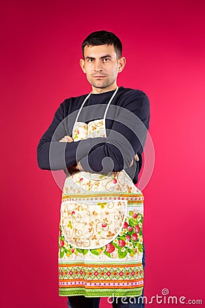 Serious young man in a kitchen apron on a pink background. The concept of gender stereotypes Stock Photo