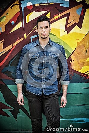 Serious young man standing against colorful graffiti wall Editorial Stock Photo