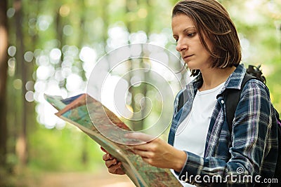 Serious young woman looking at the map and navigating while hiking through lush green forest Stock Photo