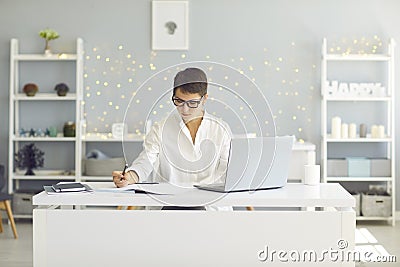 Serious young woman focusing on work or study sitting at desk with laptop at home Stock Photo