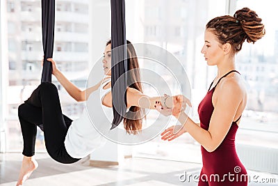 Serious young woman trainer teaching beautiful girl doing aerial yoga Stock Photo