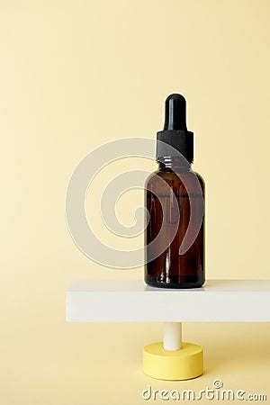 Serum facial moisturizer bottle standing on abstract pedestal on pastel yellow background with copy space, front view. Blank brown Stock Photo