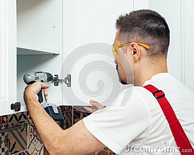 Service contractor using electric screwdriver while installing new furniture in kitchen Stock Photo