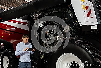 Serviceman with digital tablet on a next to ombine harvester with open hood.. Stock Photo